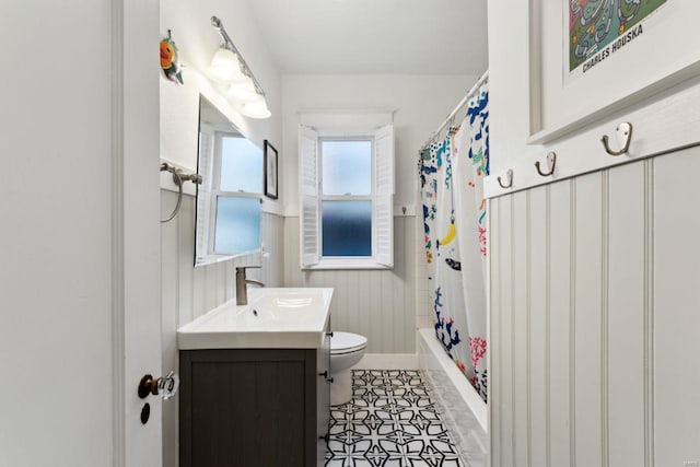 bathroom with wainscoting, toilet, tile patterned floors, shower / bathtub combination with curtain, and vanity