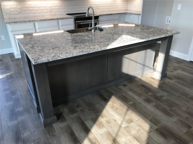 kitchen featuring tasteful backsplash, white cabinetry, sink, light stone countertops, and a center island with sink