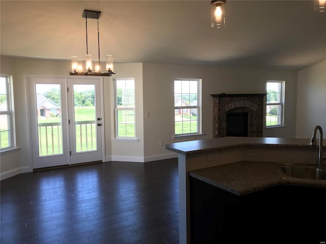 kitchen with sink, an inviting chandelier, dark hardwood / wood-style floors, a brick fireplace, and decorative light fixtures