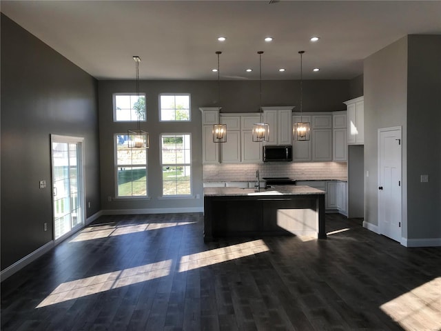 kitchen with decorative light fixtures, white cabinetry, an island with sink, dark hardwood / wood-style flooring, and light stone countertops