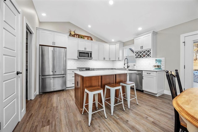 kitchen featuring lofted ceiling, a center island, stainless steel appliances, light countertops, and white cabinetry