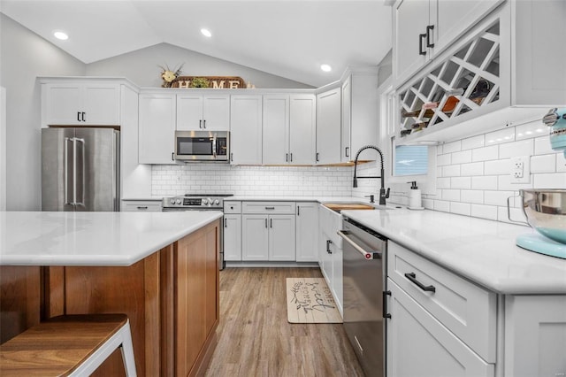 kitchen featuring appliances with stainless steel finishes, vaulted ceiling, light countertops, light wood-style floors, and white cabinetry