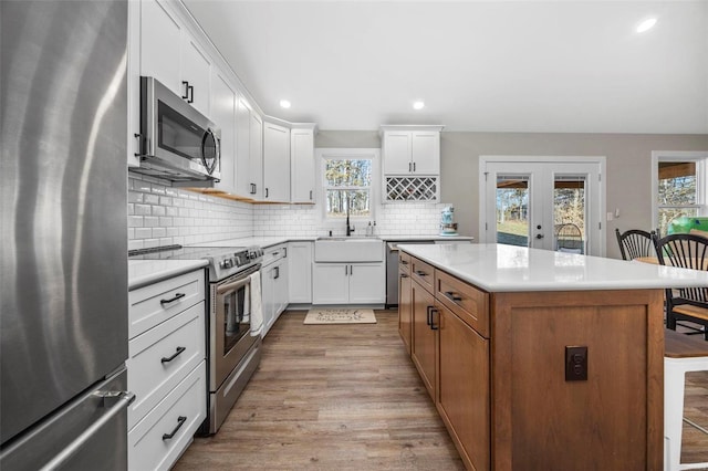 kitchen featuring stainless steel appliances, a sink, light countertops, decorative backsplash, and a center island