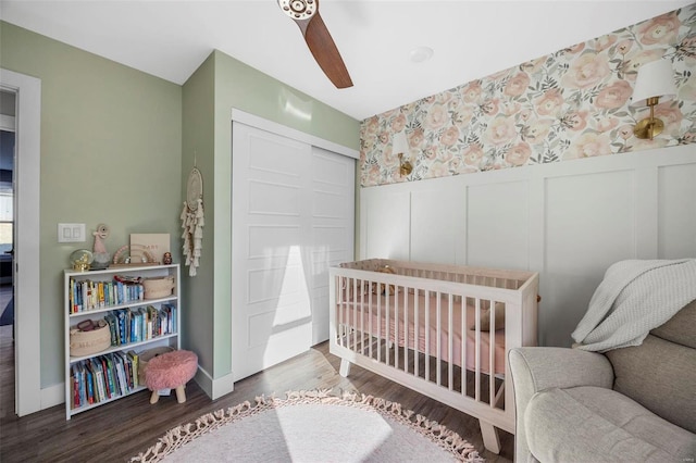 bedroom featuring a closet, wainscoting, ceiling fan, wood finished floors, and a nursery area