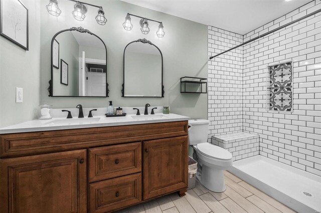 full bath featuring a sink, a tile shower, toilet, and double vanity