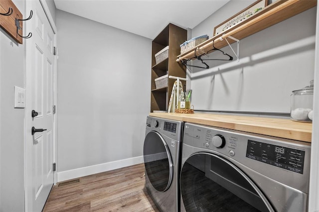 clothes washing area with visible vents, wood finished floors, washer and dryer, laundry area, and baseboards