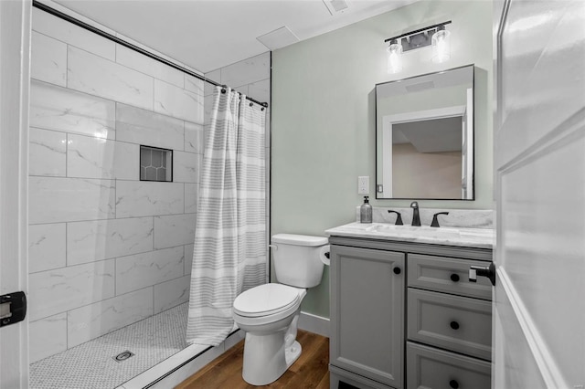 bathroom featuring toilet, a tile shower, wood finished floors, and vanity