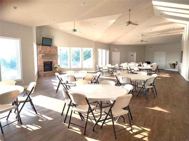 dining area featuring vaulted ceiling, plenty of natural light, wood finished floors, and a brick fireplace