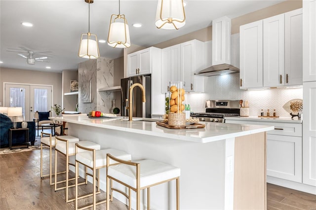 kitchen with an island with sink, appliances with stainless steel finishes, wall chimney range hood, and white cabinets