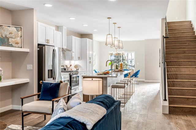 kitchen with appliances with stainless steel finishes, decorative light fixtures, white cabinets, a kitchen bar, and a kitchen island with sink