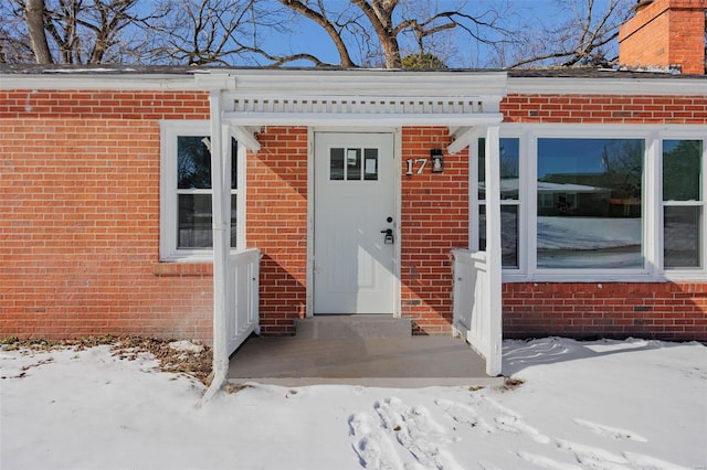 snow covered property entrance featuring brick siding