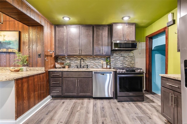 kitchen with appliances with stainless steel finishes, sink, backsplash, light stone counters, and light hardwood / wood-style floors