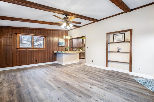 unfurnished living room featuring ceiling fan, wood-type flooring, wooden walls, and beamed ceiling