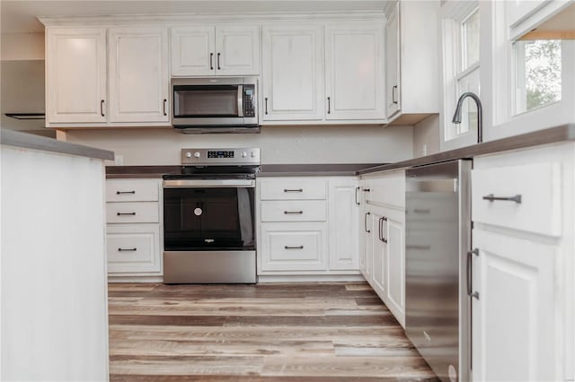 kitchen with light hardwood / wood-style floors, white cabinets, and appliances with stainless steel finishes