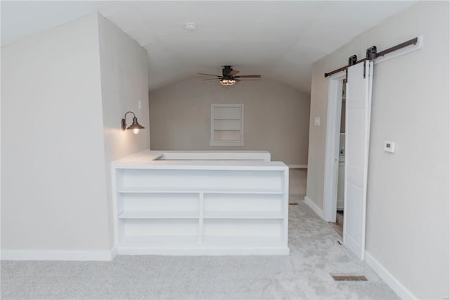 unfurnished bedroom with vaulted ceiling, a barn door, light carpet, and ceiling fan