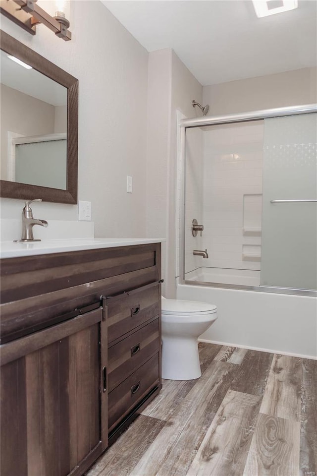 full bathroom featuring vanity, wood-type flooring, combined bath / shower with glass door, and toilet