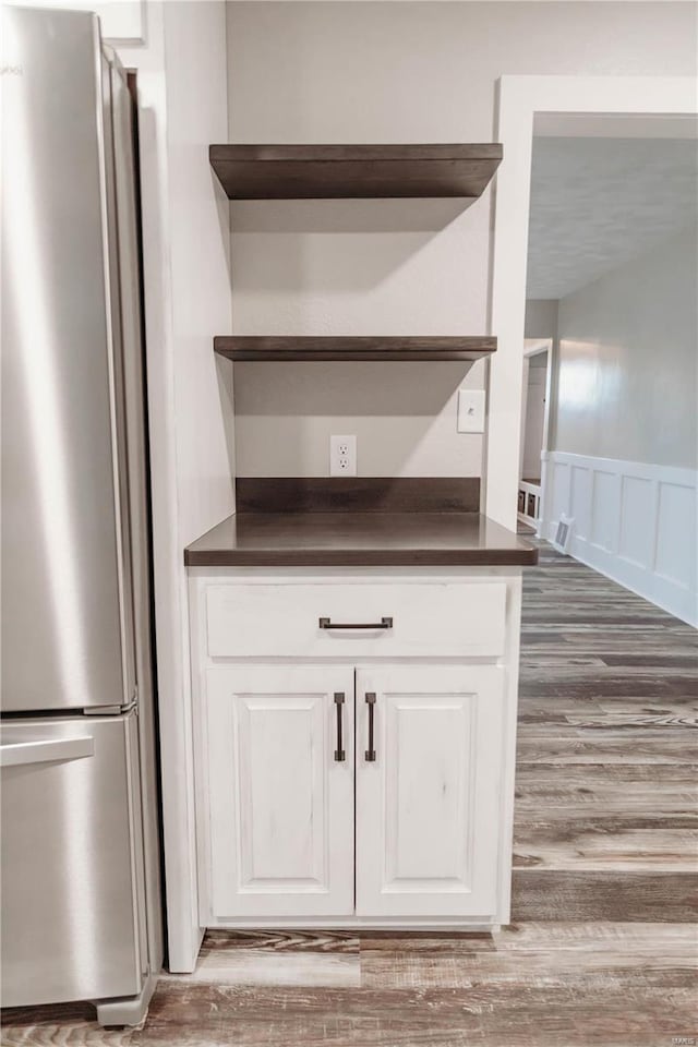 interior details with stainless steel refrigerator, white cabinetry, and hardwood / wood-style floors