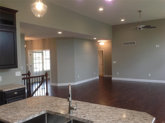 kitchen featuring dark wood-type flooring, sink, light stone counters, ceiling fan, and a kitchen island with sink