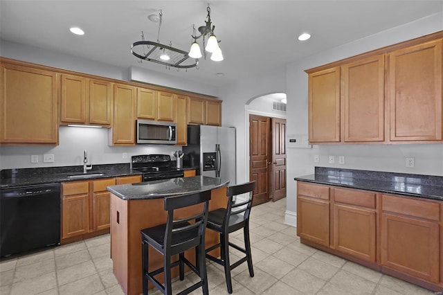 kitchen with a kitchen island, sink, a kitchen breakfast bar, dark stone counters, and black appliances