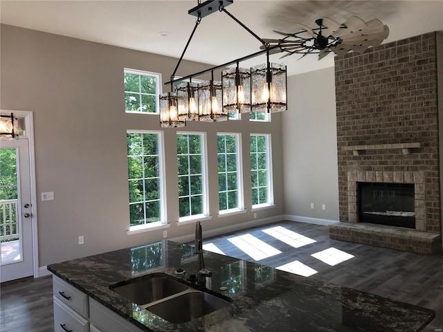 kitchen with sink, white cabinetry, a fireplace, decorative light fixtures, and dark stone counters