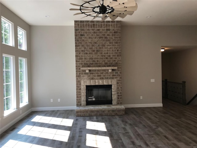 unfurnished living room with ceiling fan, a healthy amount of sunlight, a fireplace, and dark hardwood / wood-style flooring