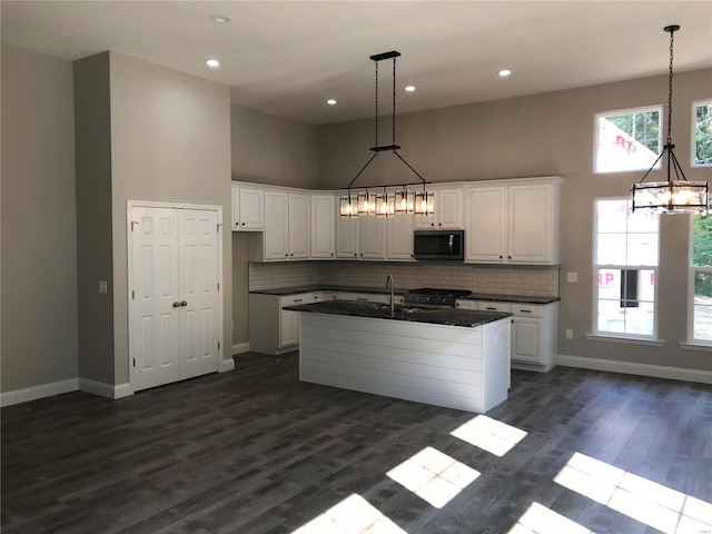 kitchen featuring tasteful backsplash, a towering ceiling, a center island with sink, and white cabinets