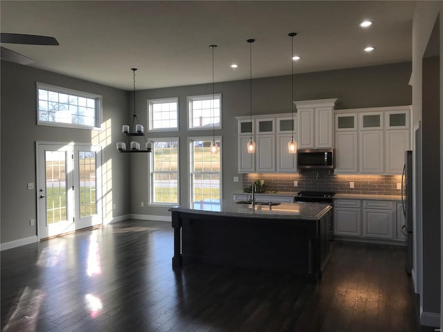 kitchen with dark hardwood / wood-style floors, sink, backsplash, white cabinets, and a center island with sink