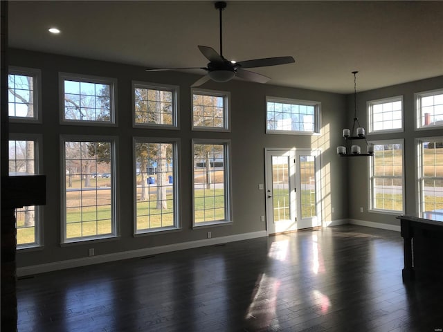 unfurnished dining area featuring a towering ceiling, dark wood-type flooring, and ceiling fan with notable chandelier