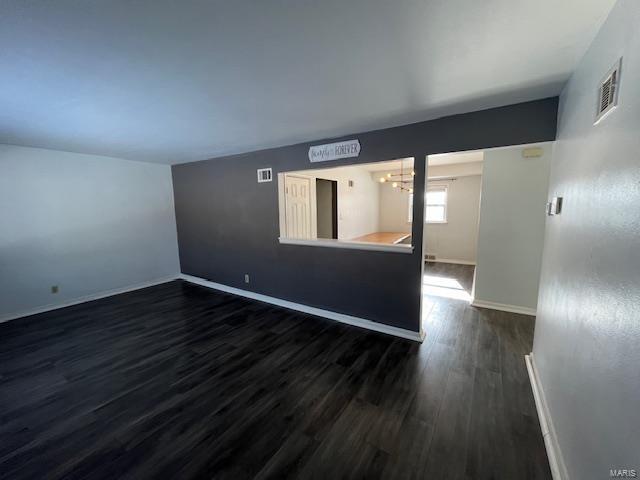 empty room with dark hardwood / wood-style flooring and a notable chandelier