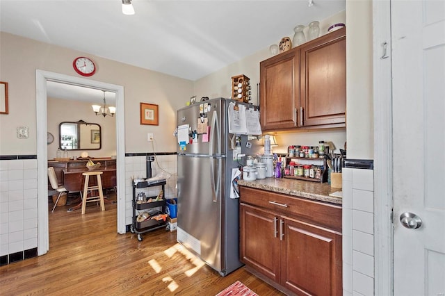 kitchen with light stone countertops, tile walls, stainless steel fridge, and light hardwood / wood-style flooring