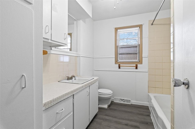 full bathroom featuring toilet, tiled shower / bath, vanity, hardwood / wood-style flooring, and decorative backsplash