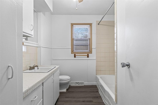 full bathroom featuring toilet, vanity, tiled shower / bath combo, hardwood / wood-style flooring, and decorative backsplash