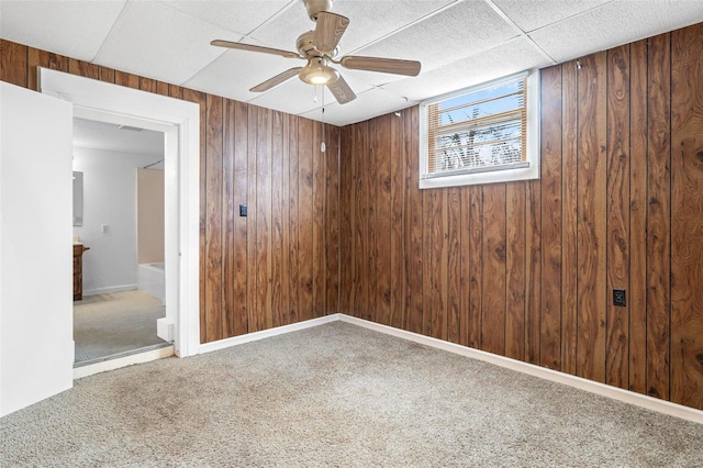 carpeted spare room featuring ceiling fan and wood walls