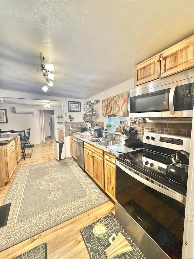 kitchen featuring appliances with stainless steel finishes, an AC wall unit, sink, light hardwood / wood-style floors, and a textured ceiling