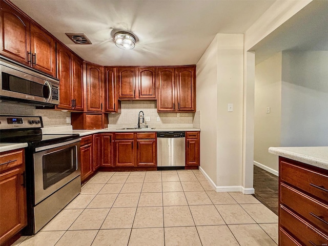 kitchen featuring light tile patterned floors, a sink, light countertops, appliances with stainless steel finishes, and decorative backsplash