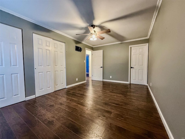 unfurnished bedroom featuring two closets, ornamental molding, ceiling fan, wood finished floors, and baseboards