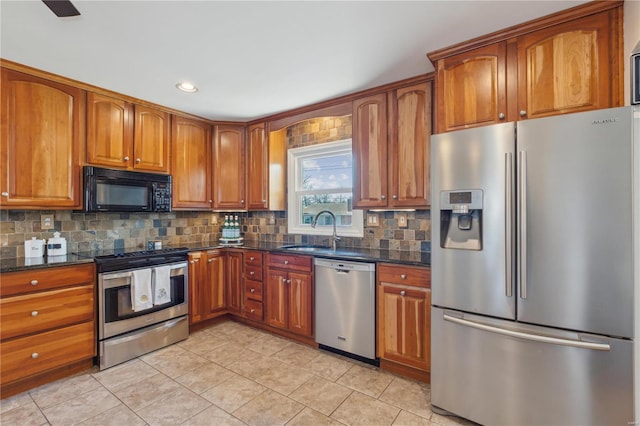 kitchen featuring dark stone counters, brown cabinets, a sink, stainless steel appliances, and backsplash