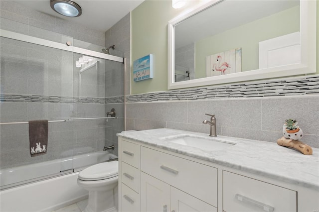 full bath featuring bath / shower combo with glass door, vanity, toilet, and tile walls