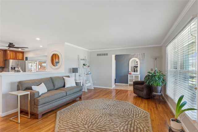 living room with crown molding, light wood finished floors, visible vents, a ceiling fan, and baseboards