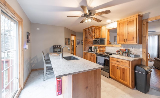 kitchen featuring sink, ceiling fan, stainless steel appliances, a kitchen island with sink, and decorative backsplash