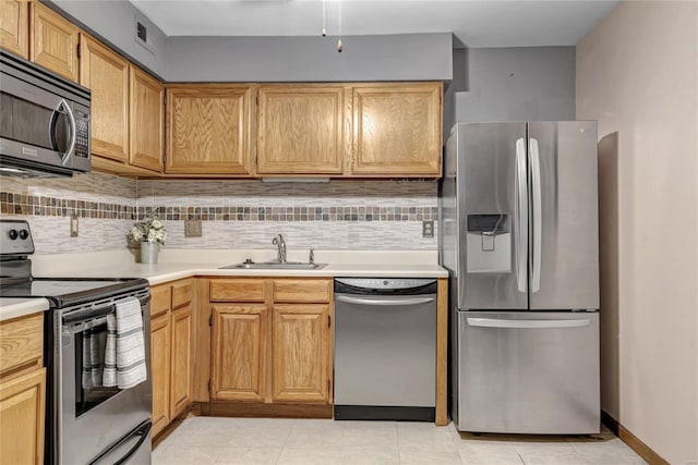 kitchen featuring stainless steel appliances, a sink, baseboards, light countertops, and tasteful backsplash