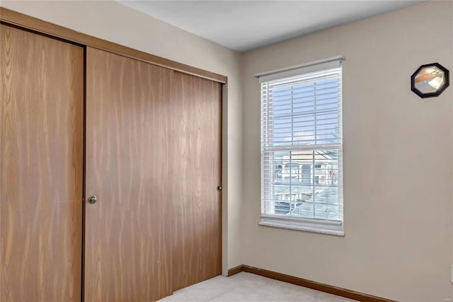 unfurnished bedroom with a closet, light colored carpet, and baseboards