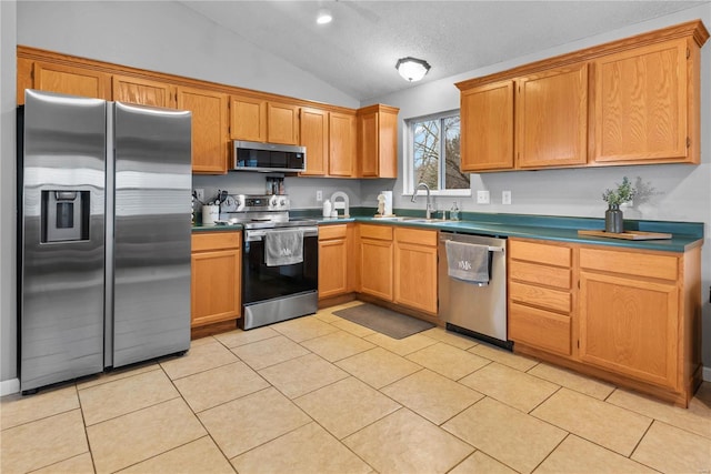 kitchen featuring sink, vaulted ceiling, a textured ceiling, light tile patterned floors, and appliances with stainless steel finishes