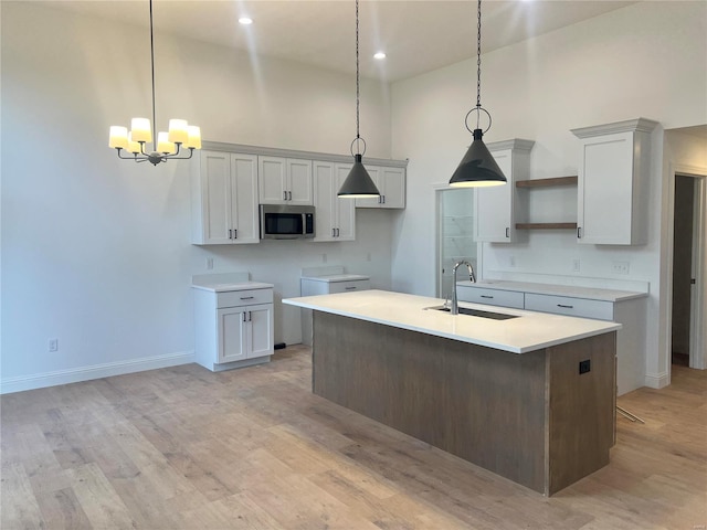 kitchen featuring an island with sink, stainless steel microwave, light wood-style floors, open shelves, and a sink