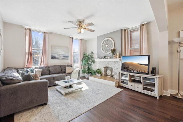 living room with a brick fireplace, baseboards, dark wood-style flooring, and ceiling fan