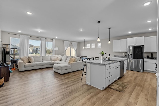 kitchen with white cabinetry, stainless steel appliances, light stone countertops, and a kitchen island with sink