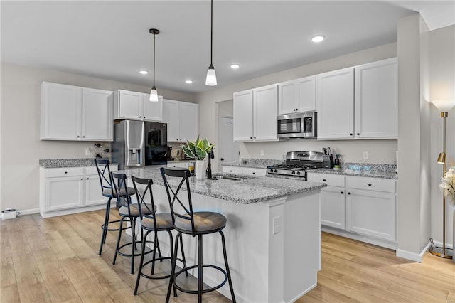 kitchen with sink, appliances with stainless steel finishes, a kitchen island with sink, light hardwood / wood-style floors, and white cabinets