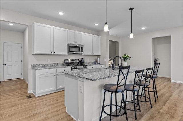 kitchen with white cabinetry, appliances with stainless steel finishes, light stone countertops, and a center island with sink