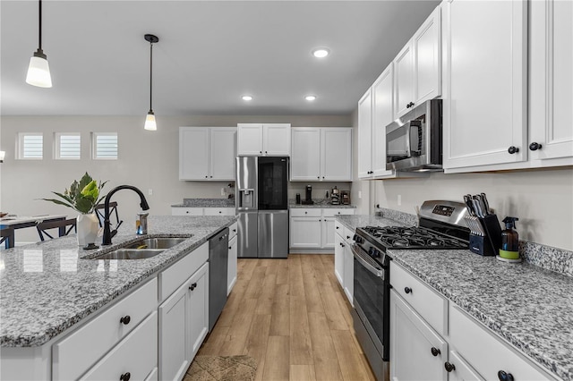 kitchen featuring sink, hanging light fixtures, a center island with sink, appliances with stainless steel finishes, and white cabinets