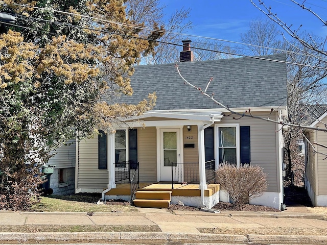 bungalow with covered porch, a shingled roof, and a chimney